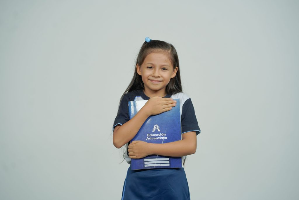 A young girl smiles while holding her school notebook, representing joy in education.
