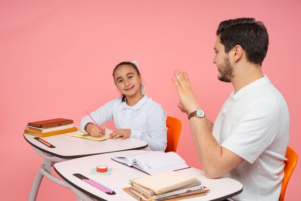 A teacher and student engaging in a classroom lesson with a pink background.