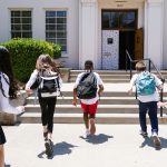 Group of students with backpacks running into school, captured from behind, showing excitement.
